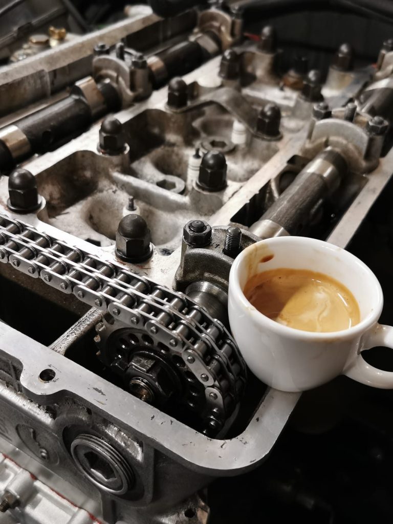 Was Sie von GAM erwarten dürfen Eine Tasse italienischer Espresso steht auf einem offenen Motorblock mit sichtbarem Motorinnenteil.